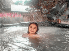 a little girl is swimming in a pool with a sprinkler in the background .