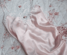 a pink satin slip with white lace trim sits on a bed