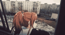 a girl with red hair is looking out a window at a city .