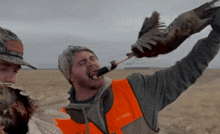 a man in an orange vest is holding a pheasant in his hand