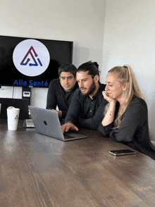 three people are looking at a laptop in front of a sign that says alia santé