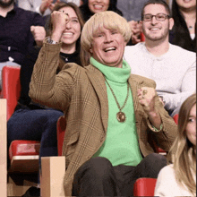 a man wearing a green turtleneck and a plaid jacket is sitting in a crowd