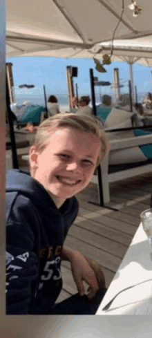 a young boy wearing a blue sweatshirt with the number 5 on it is smiling while sitting at a table .