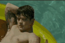 a shirtless man is floating on a yellow raft in the water