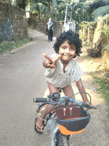 a little girl is riding a bike and giving a peace sign