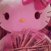 a pink hello kitty stuffed animal is holding a pile of money