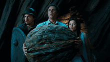 a man and two women are holding a large walnut in a dark room .