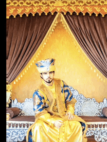 a man in a yellow and blue costume is sitting in front of a curtain