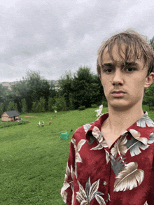 a young man in a hawaiian shirt stands in a field