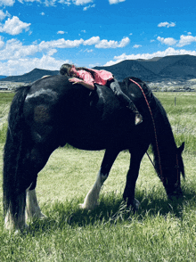 a girl laying on the back of a black horse in a field