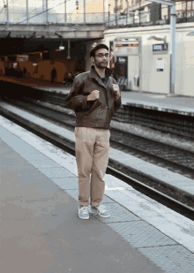 a man in a brown jacket stands on a train platform with a sign that says ' a ' on it