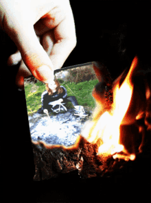 a person is holding a picture of a woman sitting on a rock next to a fire