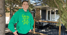 a boy wearing a green hoodie that says call 25 2019 is standing in front of a house .