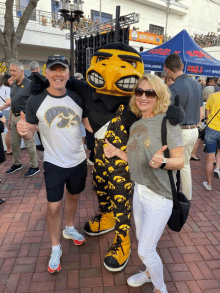 a man and a woman pose with a mascot wearing a iowa shirt