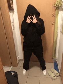 a woman wearing a black hoodie stands in a hallway with her hands on her face