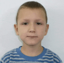 a young boy wearing a blue and gray striped shirt looks at the camera