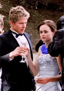 a man in a tuxedo and bow tie holds a glass of champagne next to a woman in a white dress