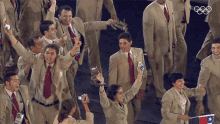 a group of people in suits and ties are cheering and holding flags with the olympics logo in the background