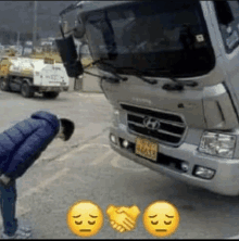 a man is bending down in front of a truck and shaking hands with it .