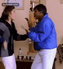 a man in a blue jacket is dancing with a woman in white pants .