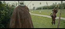 a man in a brown cape is walking in a park with a tree in the background .