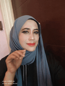 a woman wearing a hijab is taking a selfie on a vivo x50 phone