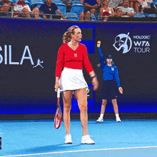 a woman holding a tennis racquet stands on a tennis court in front of a sign that says wta tour