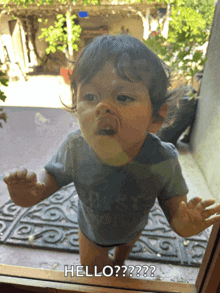 a baby standing in front of a glass door with the words hello written on it