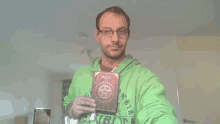 a man in a green columbia sweatshirt holds up a book titled spells