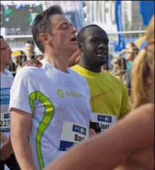 a man wearing a white shirt with the word scott on it stands next to another man wearing a yellow shirt