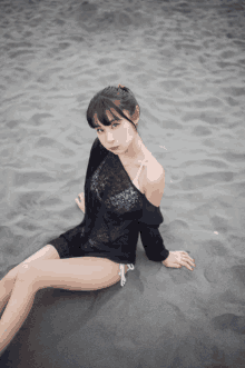 a woman in a black dress sits on the beach