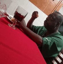 a man in a green nike shirt sits at a table holding a glass of red wine