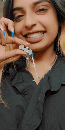 a woman wearing a black shirt is smiling and holding a necklace with a bat pendant