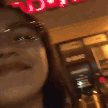 a woman wearing glasses is standing in front of a store with a red sign on the top of it .