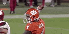 a football player wearing a helmet with a paw print on it is standing on a field with his fist in the air .