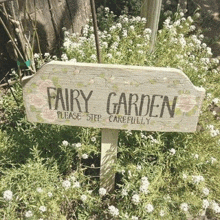 a wooden sign in a garden that says fairy garden please step carefully .