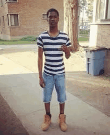 a man wearing a striped shirt and shorts is standing on a sidewalk .