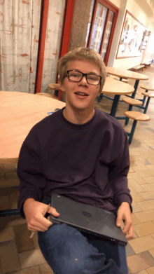 a boy wearing glasses and a purple shirt is holding a laptop