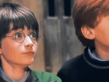 a boy wearing glasses and a green sweater looks up at something