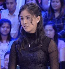 a woman is sitting in front of a crowd of people wearing a black top and a necklace .