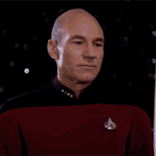 a bald man in a red uniform with a star trek badge