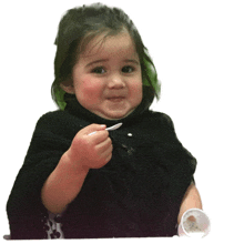 a little girl in a black sweater is eating something with a spoon