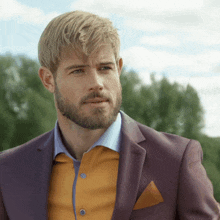 a man with blonde hair and a beard is wearing a purple suit