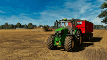 a green john deere tractor is pulling a red trailer in a field