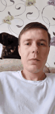 a man in a white shirt sits on a couch with a cat in the background