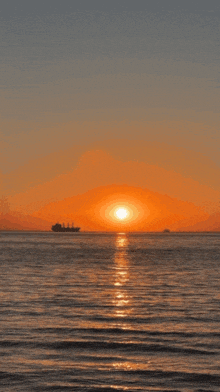 a sunset over a body of water with a ship in the distance