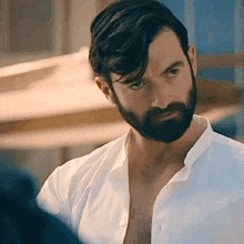 a man with a beard is wearing a white shirt and looking at the camera .