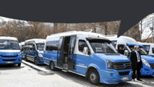 a man in a suit stands in front of a row of blue and white iveco buses