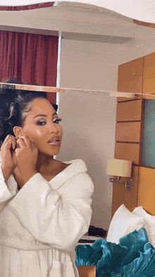 a woman in a white robe adjusts her earring in front of a mirror