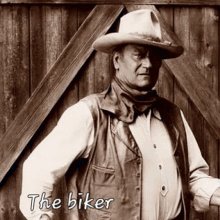 a man wearing a cowboy hat and vest is standing in front of a wooden wall with the words the biker written below him